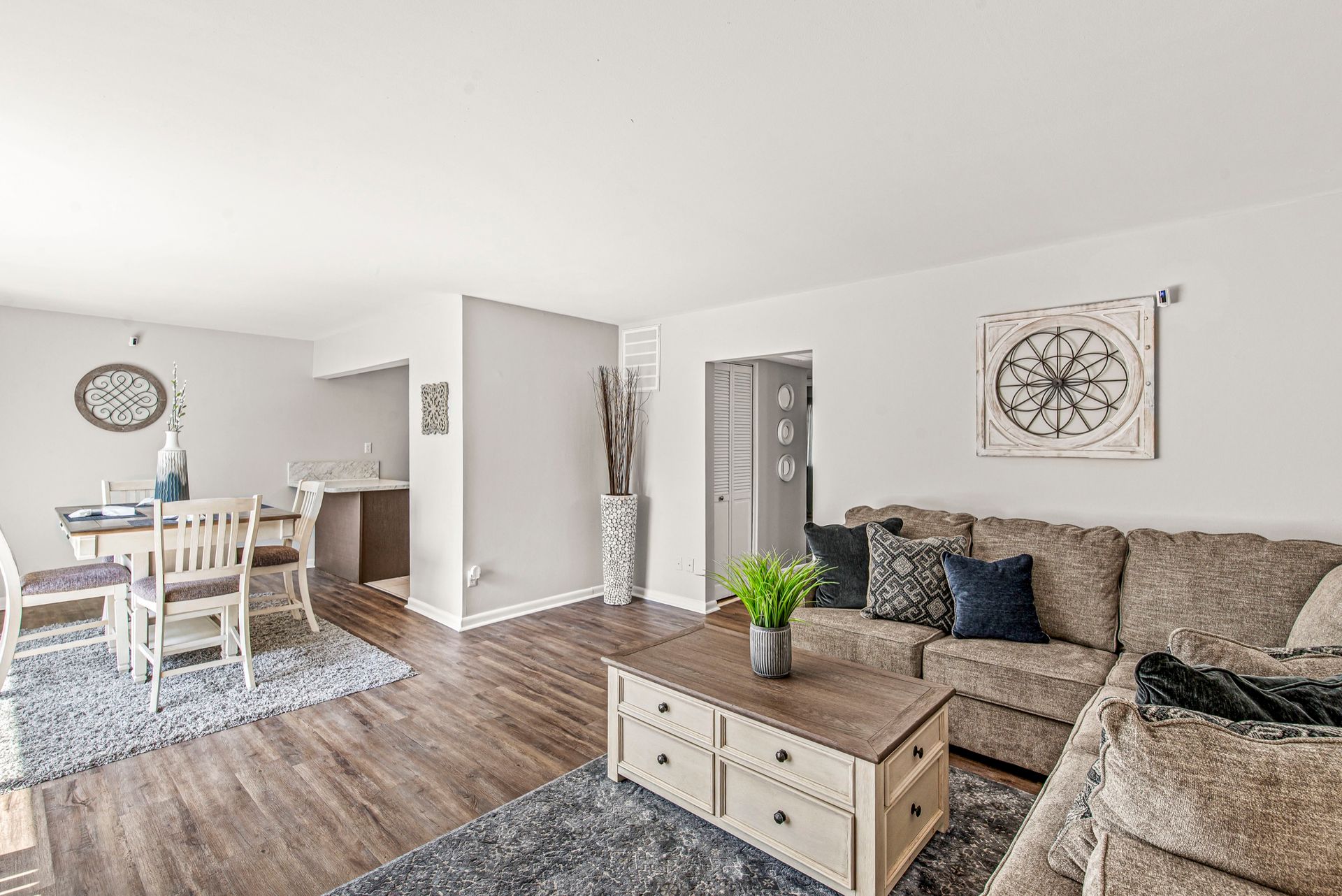 Bright living and dining area with beige sofas, wooden coffee table, dining set, wall art, and hardwood floors in a neutral-toned open layout.